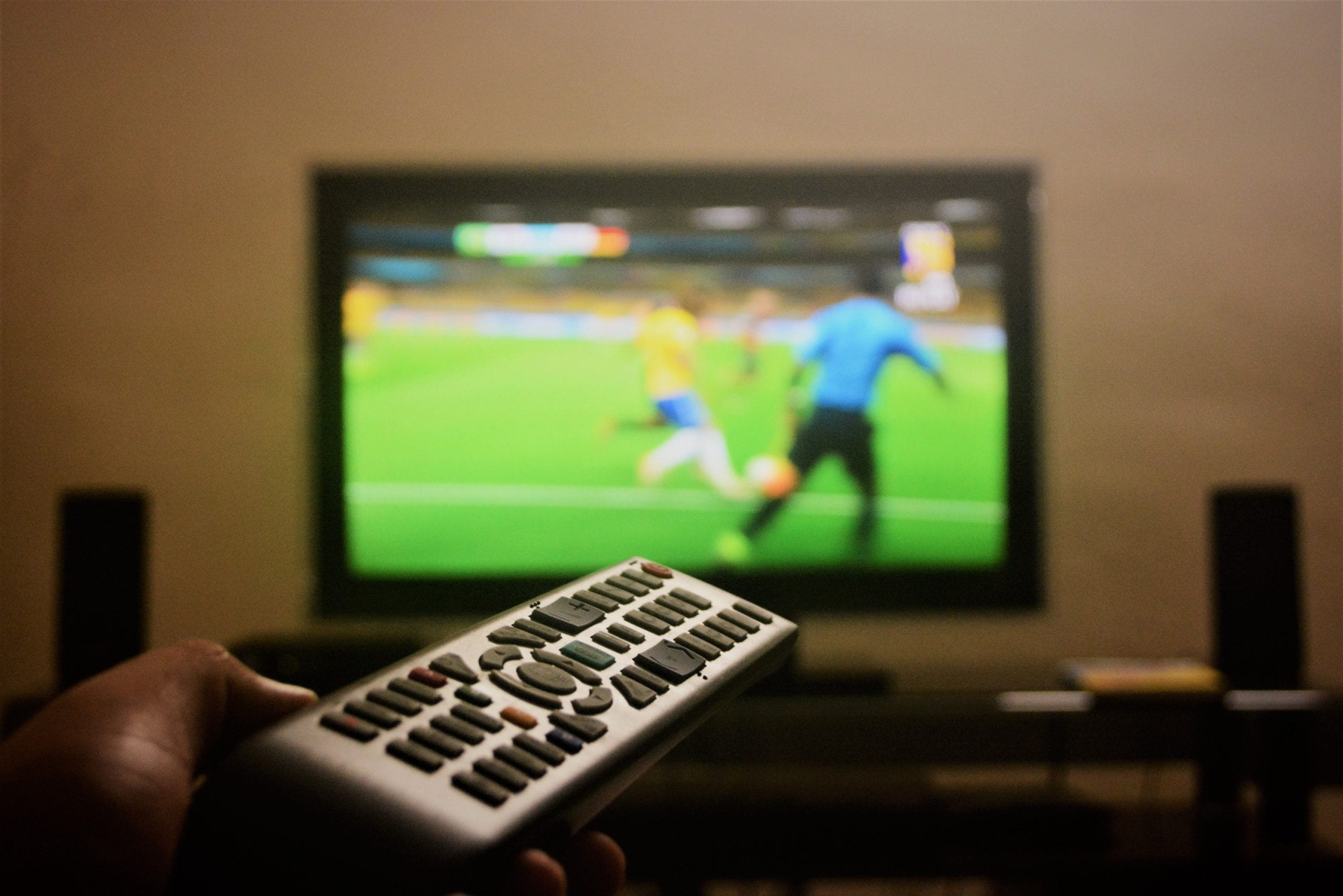 Remote control pointed at a TV showing a sports match